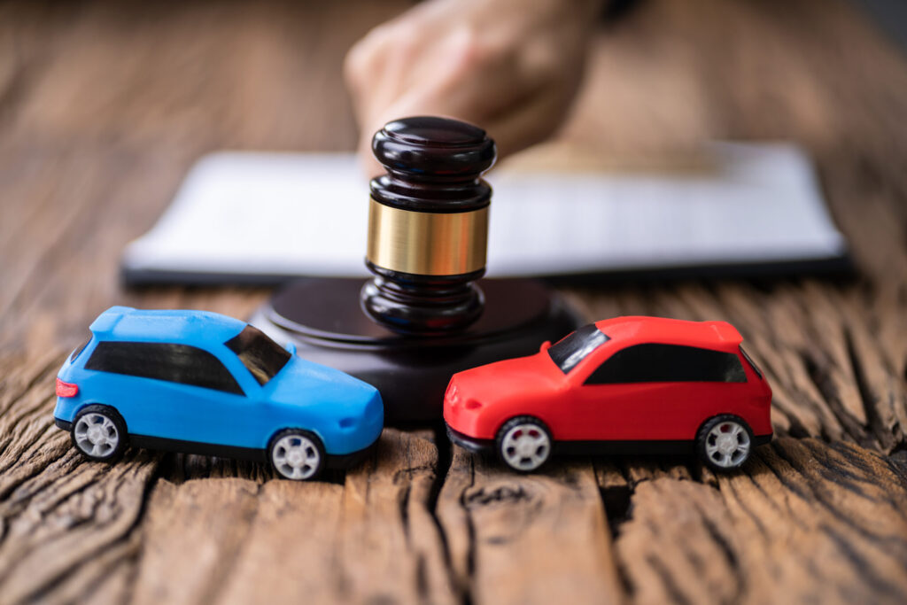 Judge&rsquo;s gavel behind two toy cars involved in a crash, symbolizing car accident liability, auto insurance claims, and personal injury litigation.