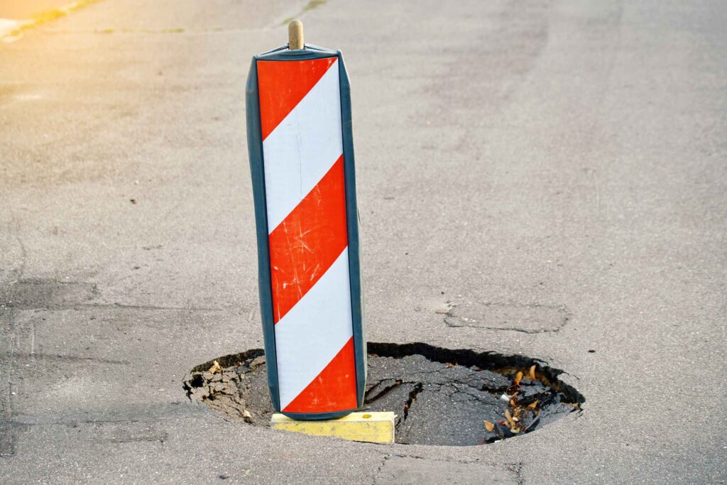 Dangerous pothole on a Pennsylvania road marked with a warning pylon, illustrating a known road hazard that can cause a motorcycle accident.